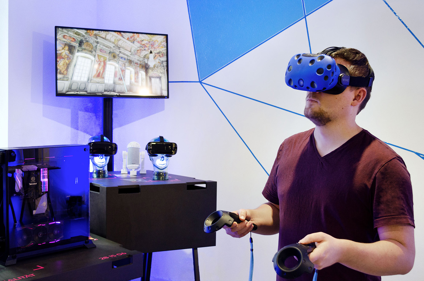 Rechts ist ein Mann abgebildet der eine Virtual Reality-Brille trägt und in der Hand je einen Controler hält. Im Hintergrund sieht man auf einem Bildschirm was der Mann durch die Brille gerade sieht.